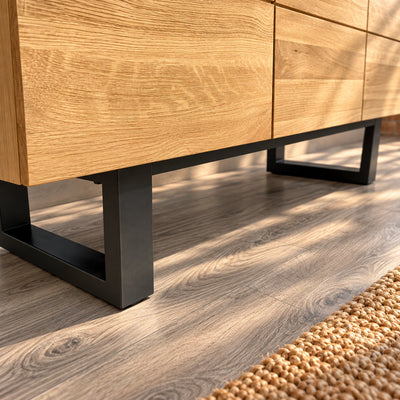 Close-up of the Fusion oak sideboard's dark metal loop legs beneath the oak cupboard doors.
