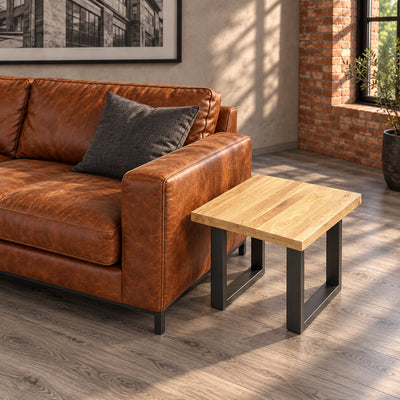 Elevated view of the Fusion oak lamp table's square tabletop and two separate metal loop bases next to a cognac sofa.

