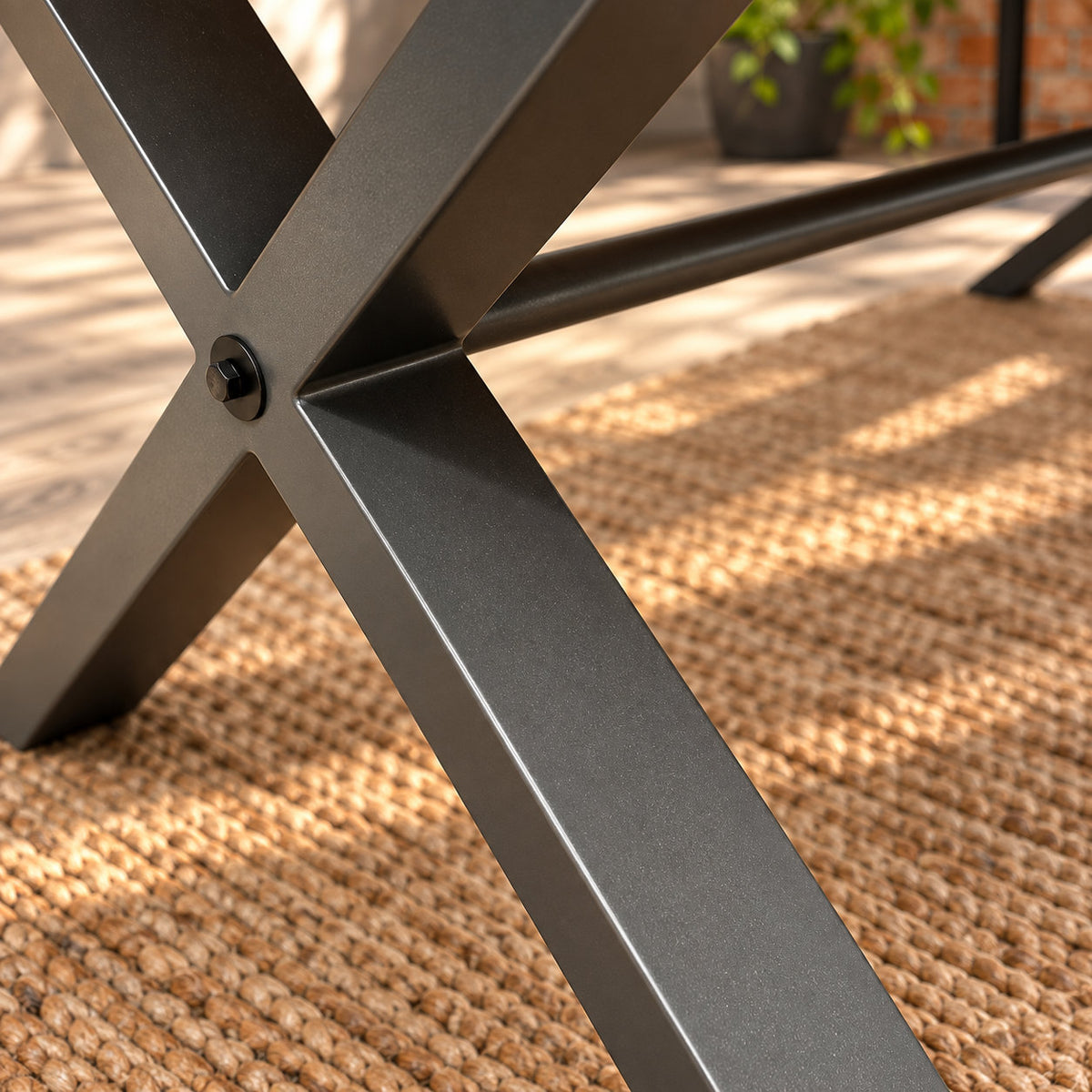 Detail of the Fusion oak large dining table’s charcoal metal cross leg and foot on a natural woven rug.